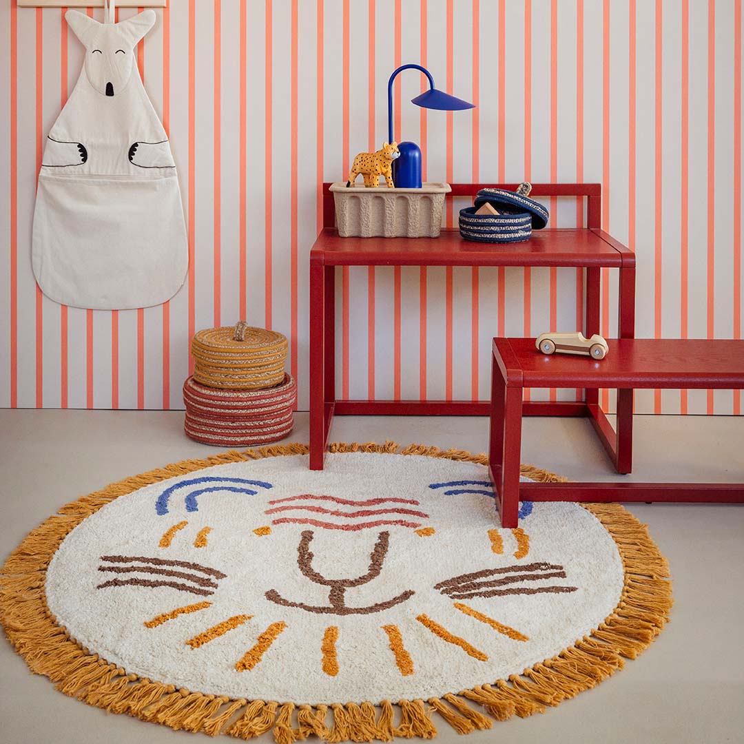 Rond vloerkleed met leeuwenkop op de vloer in een kinderkamer met rood meubilair.