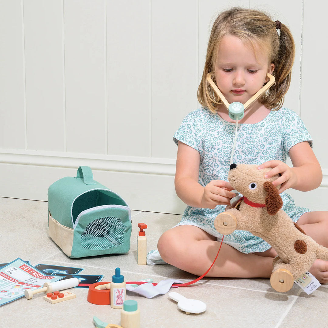 Een meisje speelt met de Tender Leaf Toys dierenarts speelset en onderzoekt een pluchen hond met een houten stethoscoop.