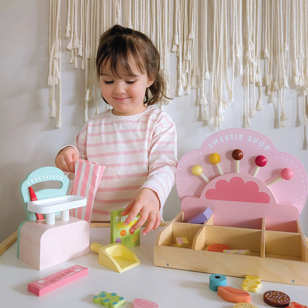 Een jong meisje speelt met de Tender Leaf Toys houten speelset snoepwinkel, met een roze kraam en weegschaal.