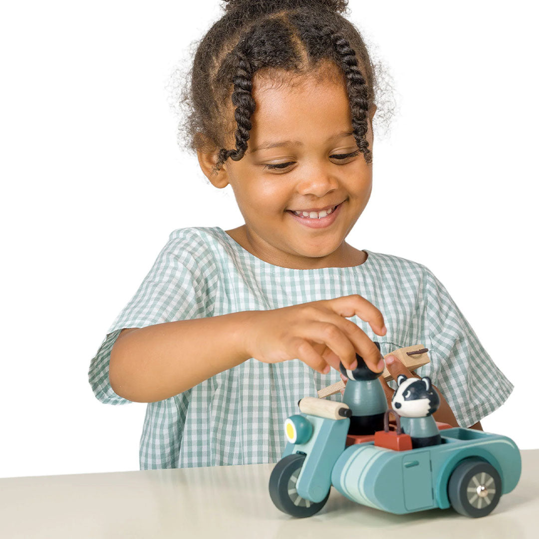 Een lachend meisje speelt met de Tender Leaf Toys houten speelset van dassen op motor.
