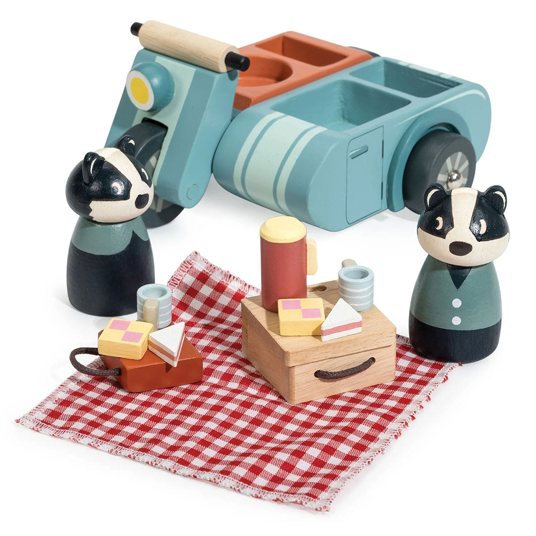 De Tender Leaf Toys houten speelset met een blauwe motor, twee dassenfiguren en alle picknickaccessoires op een geruite deken.