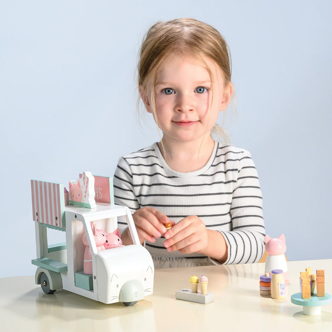 Een meisje speelt met de Tender Leaf Toys Kitty's milkshake wagen speelset op een tafel.