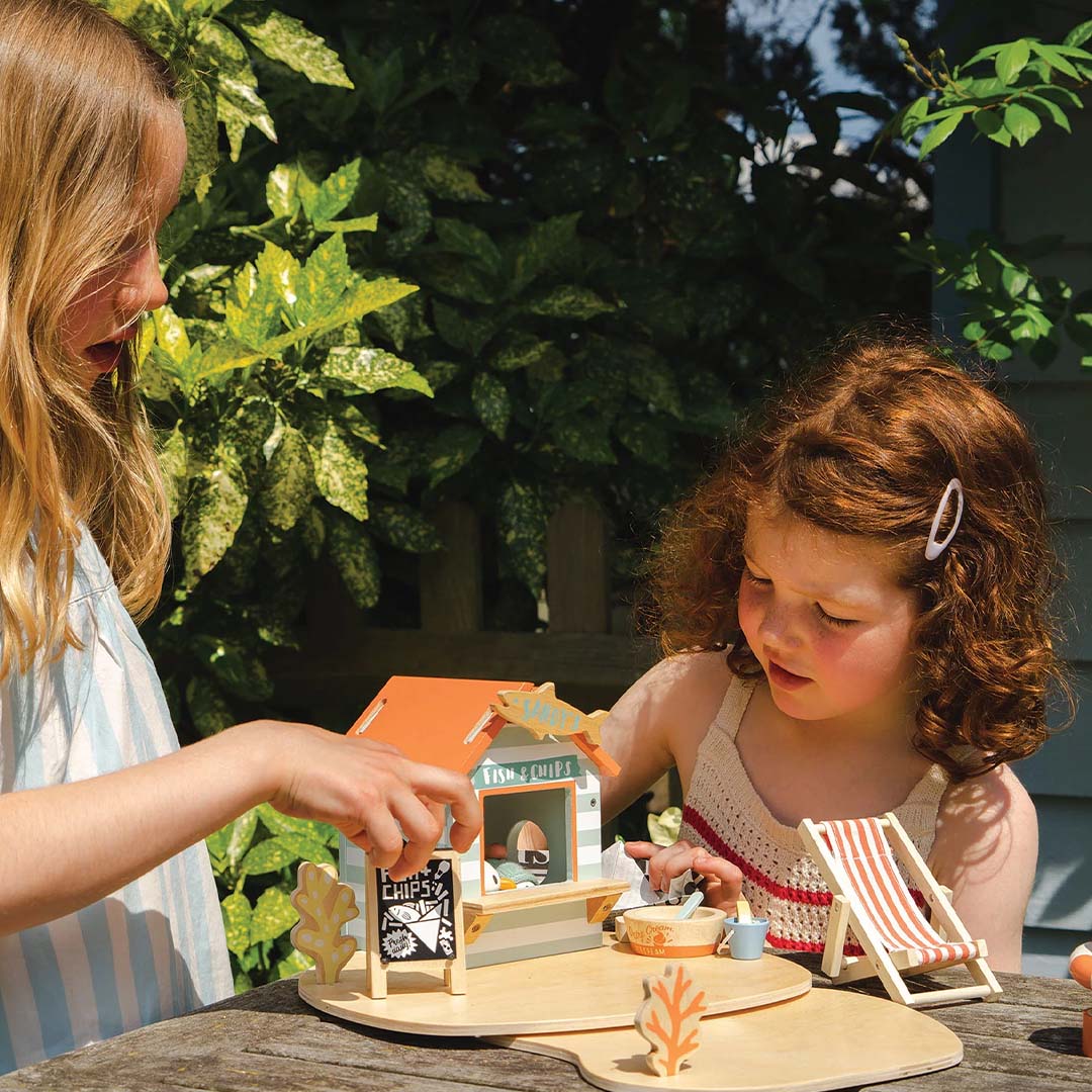 Twee meisjes spelen buiten met de Tender Leaf Toys speelset strandpaviljoen op een houten tafel.