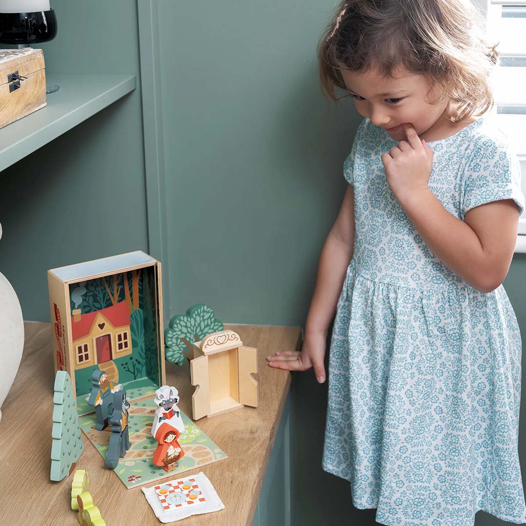 Een meisje kijkt aandachtig naar de Tender Leaf Toys Roodkapje speelset op een houten tafel.