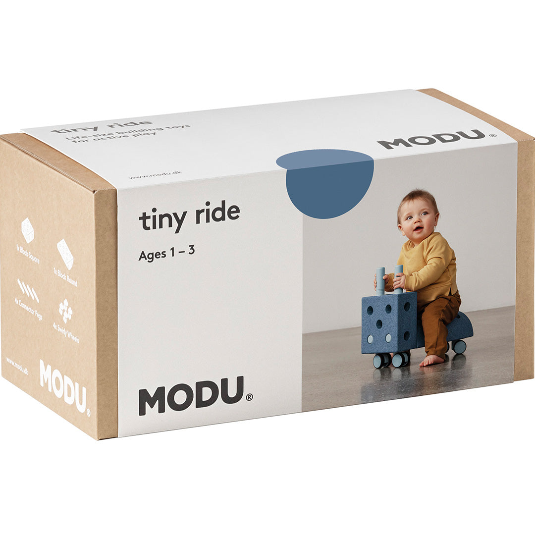 De verpakking van de Modu Tiny Ride loopwagen, met een afbeelding van een baby op het speelgoed.