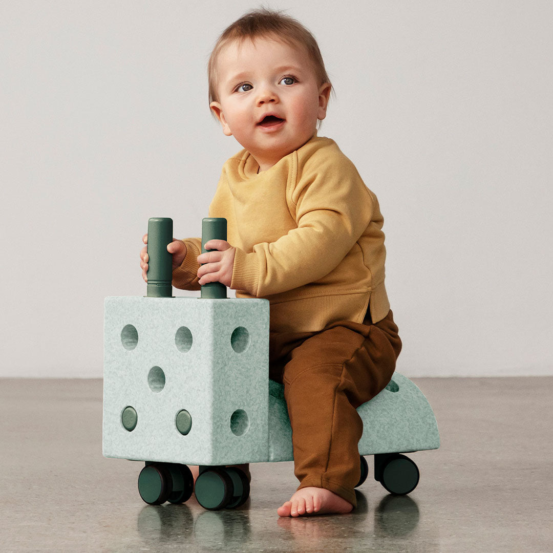 Een baby zit op een modu rijdier gemaakt van mintkleurige schuimrubberblokken.