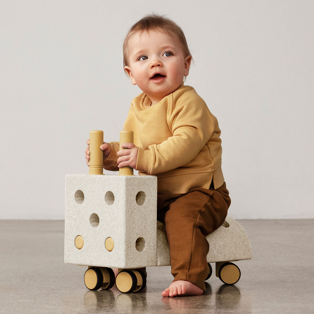 Baby zit op een Modu loopwagen gemaakt van beige schuimrubber blokken met gele details.