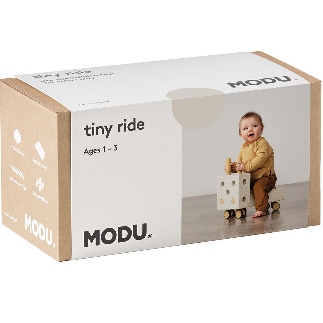 De verpakking van de Modu Tiny Ride loopwagen, met merknaam en een foto van een baby op het speelgoed.