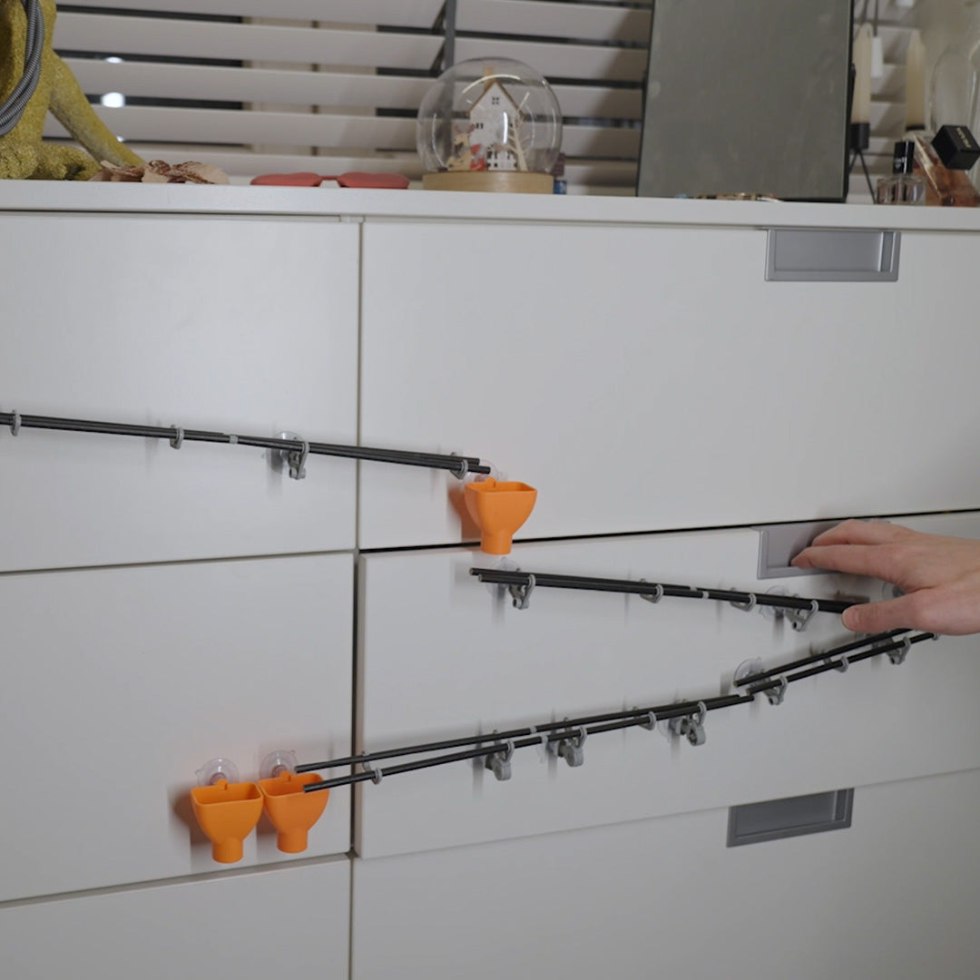 Een marblelous knikkerbaan met oranje trechters en zwarte stangen op een witte kast, waarbij een hand de baan aanpast.