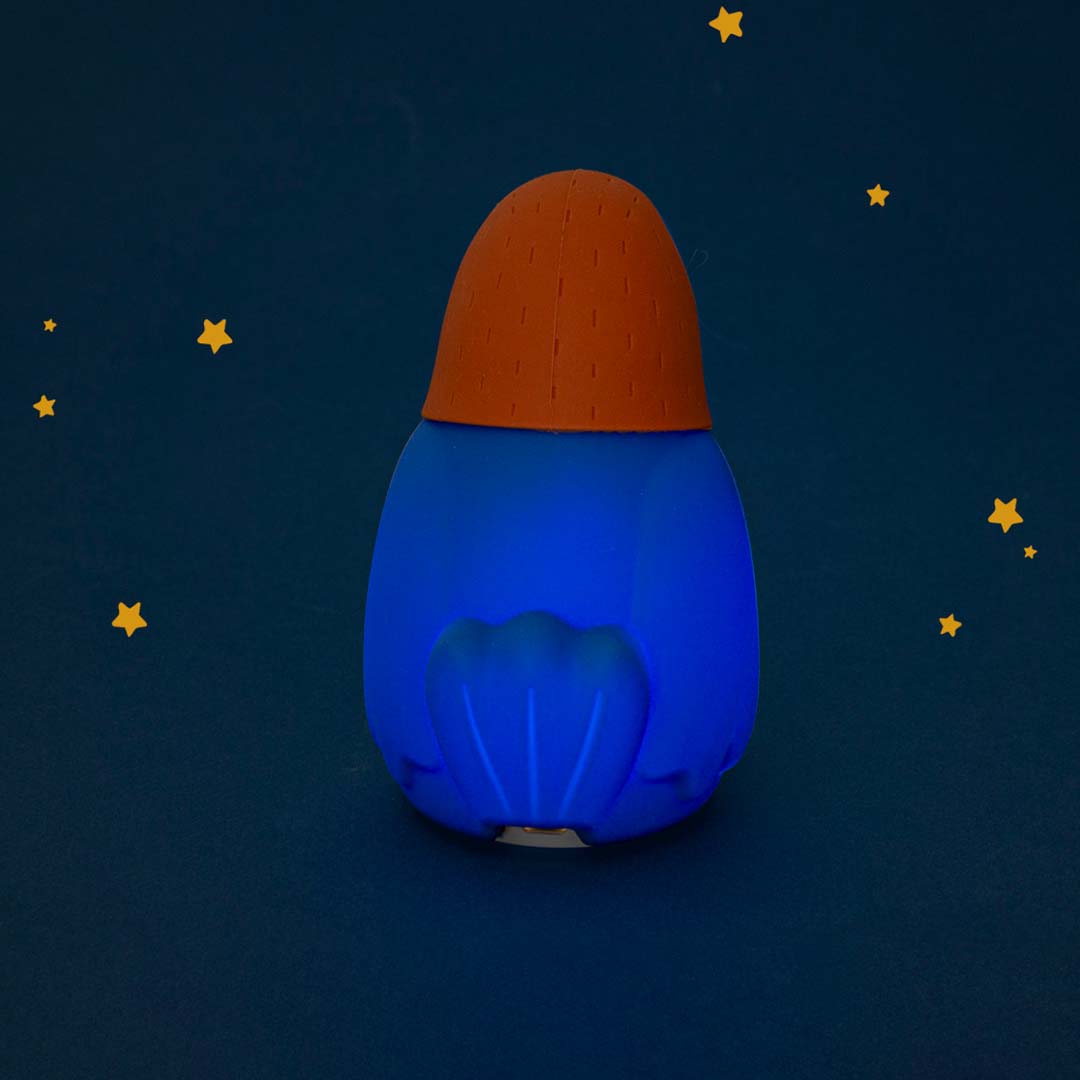 Moulin Roty nachtlampje in de vorm van een neushoornvogel, van achteren gezien, dat blauw licht geeft tegen een donkere achtergrond met sterren.