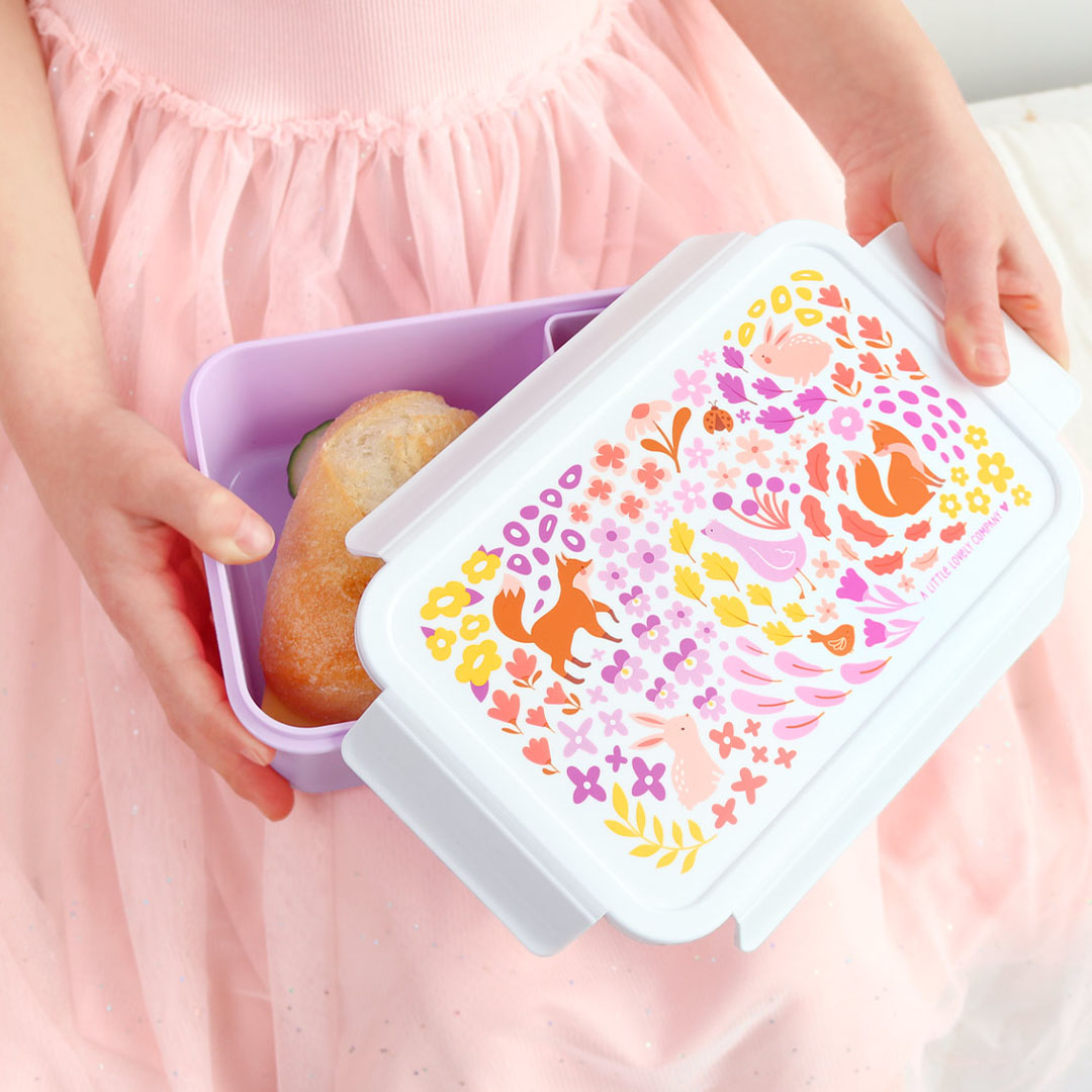Een kind houdt een open paarse bento broodtrommel met bloemen- en dierenpatroon vast, gevuld met een broodje.