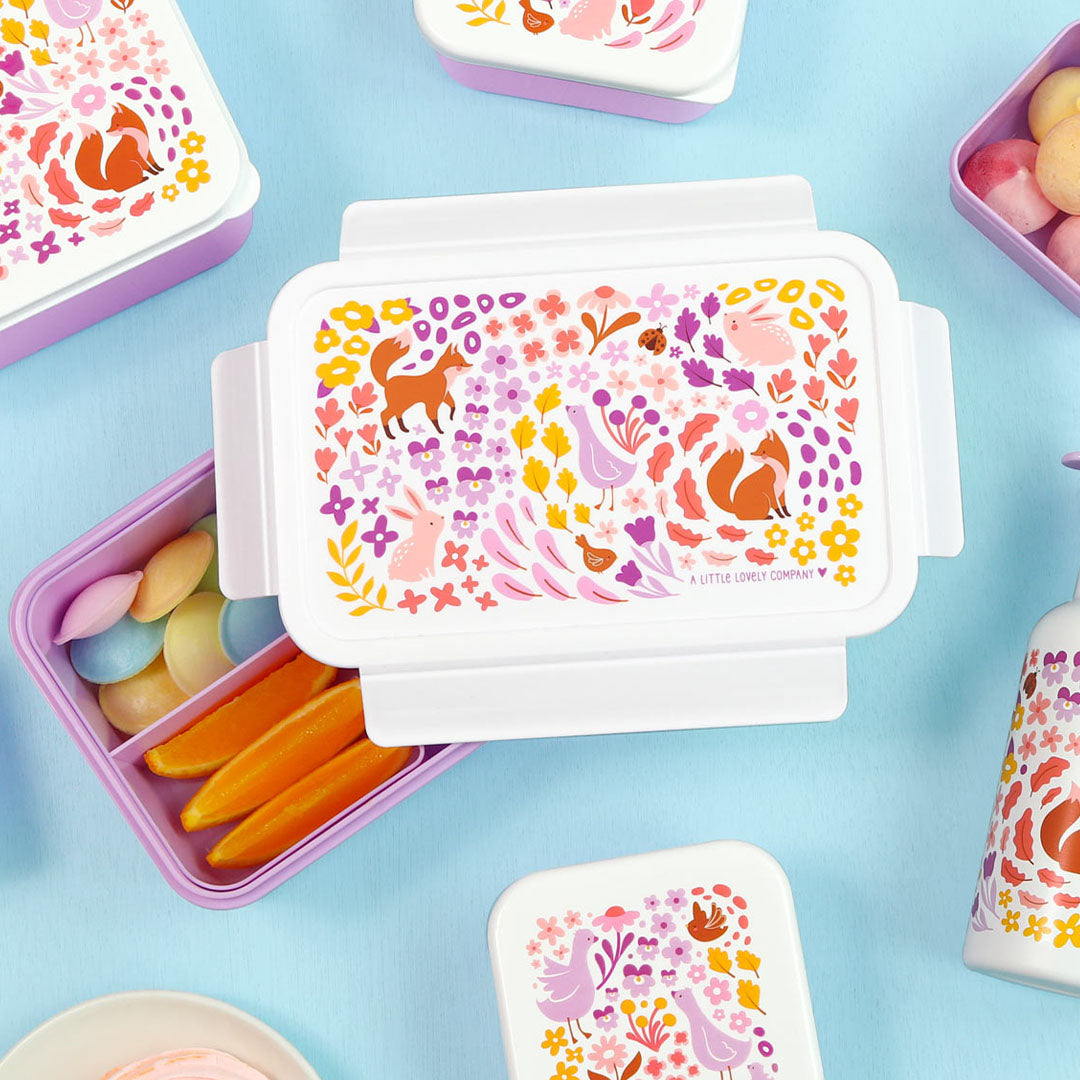 Meerdere paarse bento broodtrommels en kleine containers met bloemen- en dierenpatroon, gevuld met snacks.
