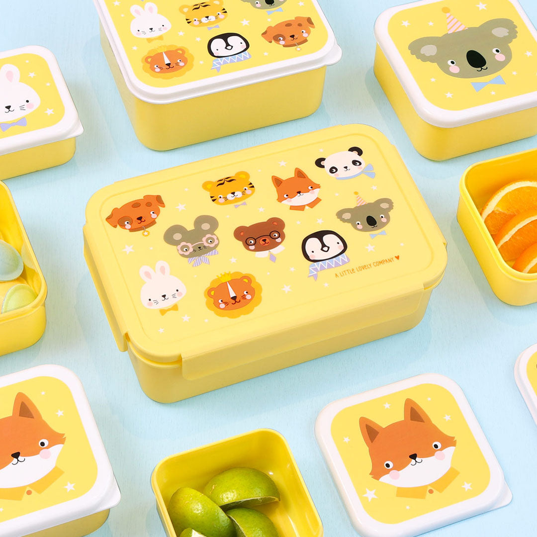 Een collectie van gele A Little Lovely Company broodtrommels en kleine lunchcontainers met dierenvrienden, sommige gevuld met fruit.