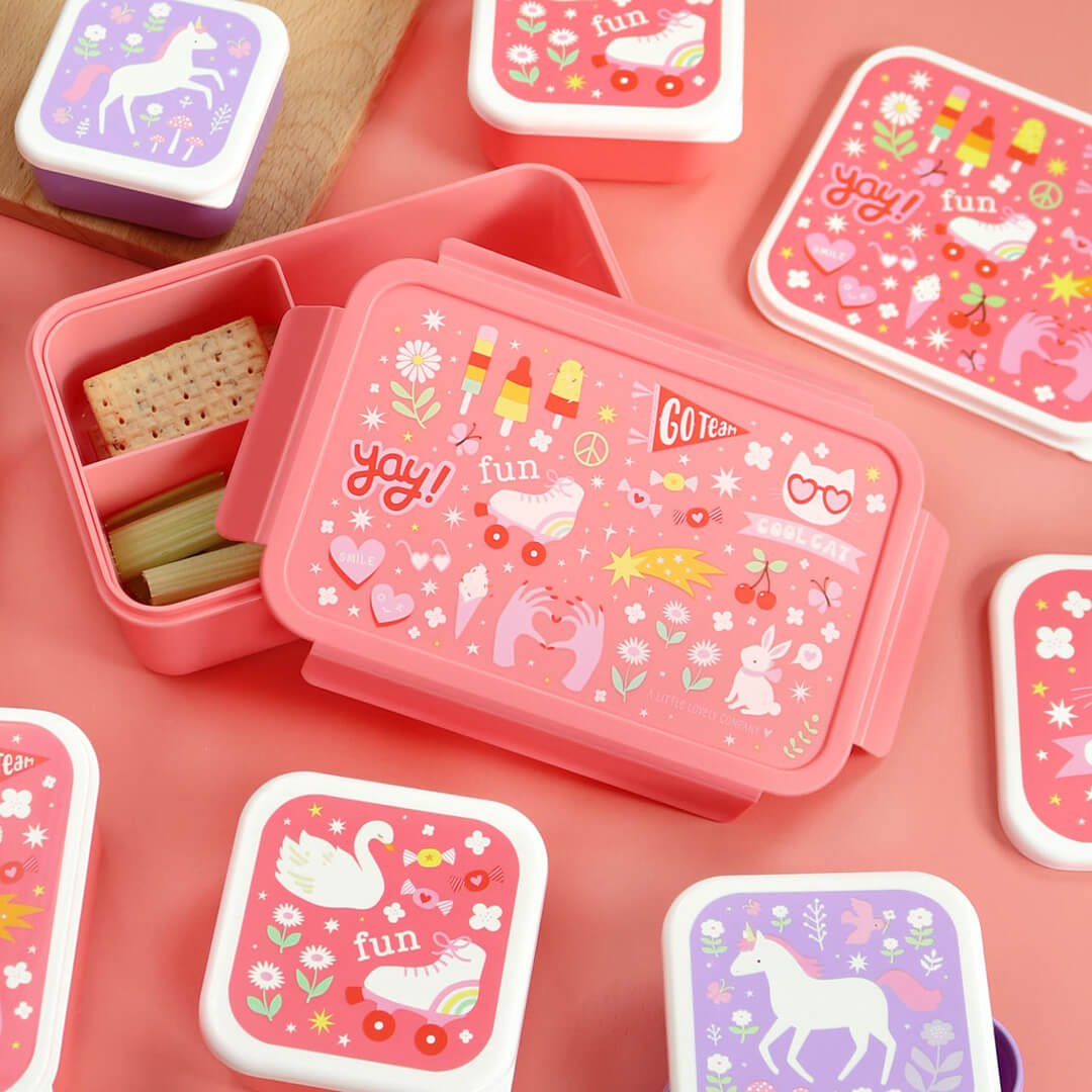 a little lovely company roze broodtrommel met 'fun' thema, open met crackers en selderij, omringd door bijpassende snackdoosjes.