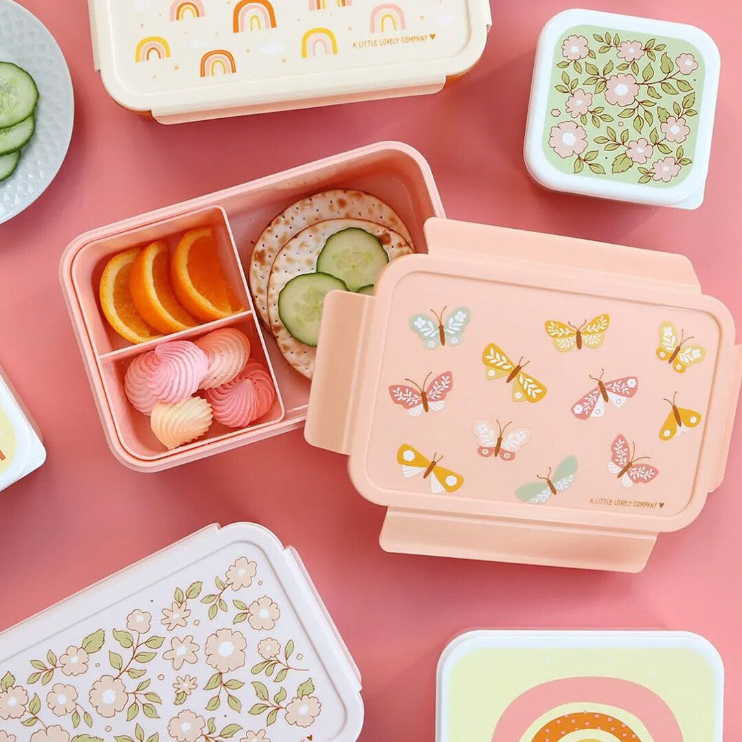 Overzicht van diverse A little lovely company kinderbroodtrommels en snackdoosjes met vlinder-, regenboog- en bloemenpatronen, gevuld met eten.
