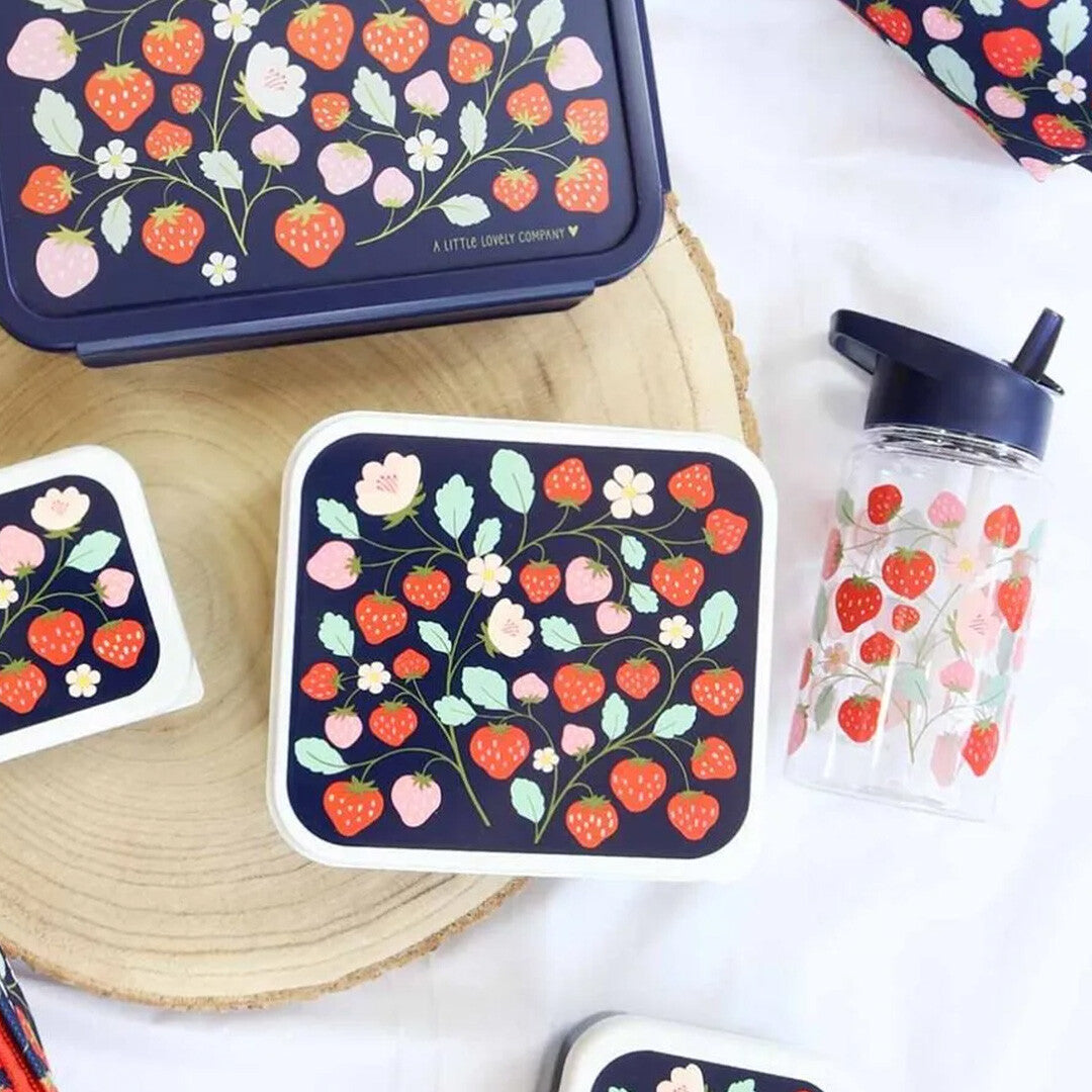 A little lovely company drinkfles met rietje voor kinderen met aardbeienpatroon, samen met bijpassende lunchboxen op een houten ondergrond.
