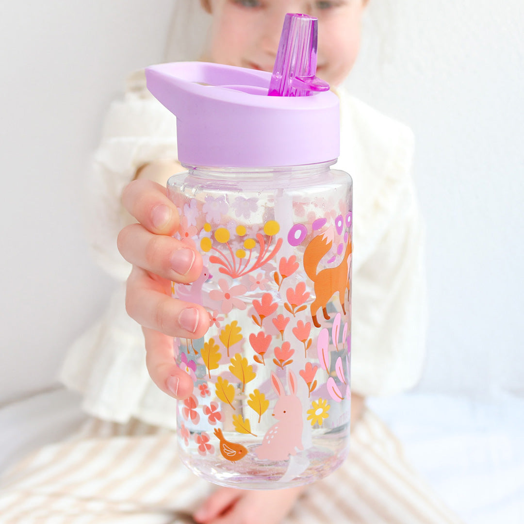 Een kind houdt de a little lovely company drinkfles met rietje met bloemen- en dierenpatroon vast.