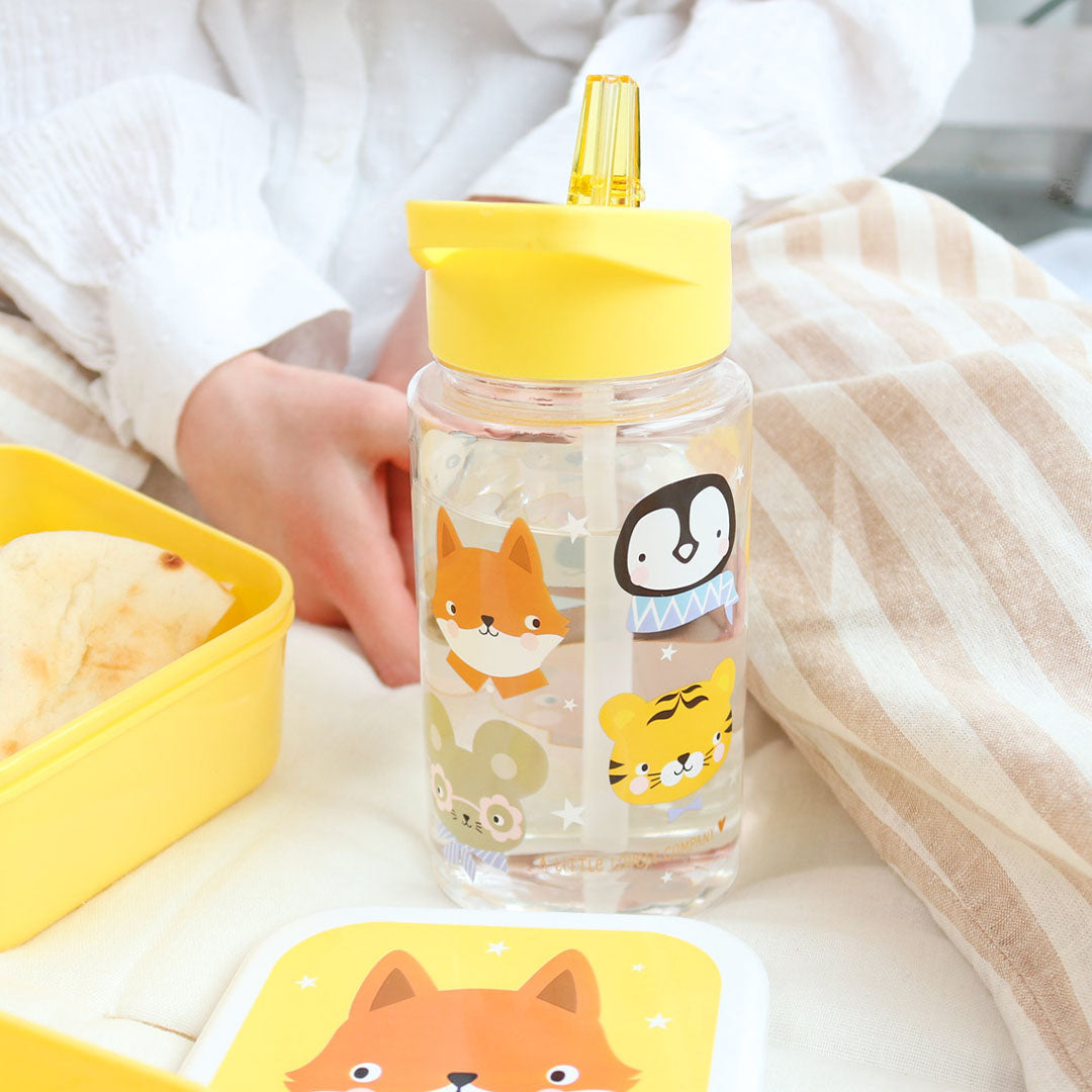 Een a little lovely company kinderwaterfles met dierenvriendenprint en gele dop, gevuld met water, naast een gele lunchbox.