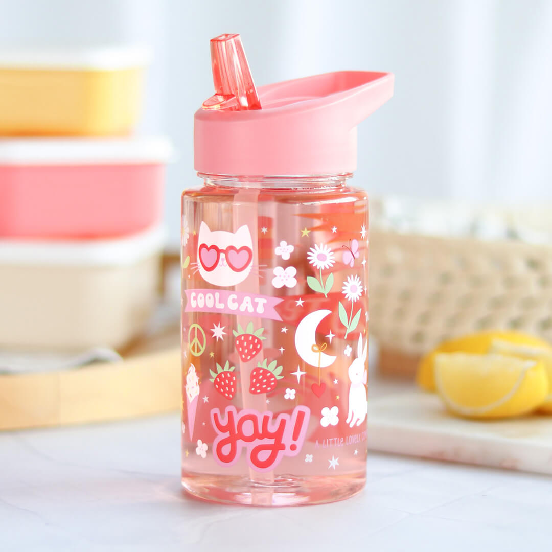 De a little lovely company kinderdrinkfles met roze deksel en rietje, gevuld met roze vloeistof, staat op een tafel met lunchboxen en citroenen.