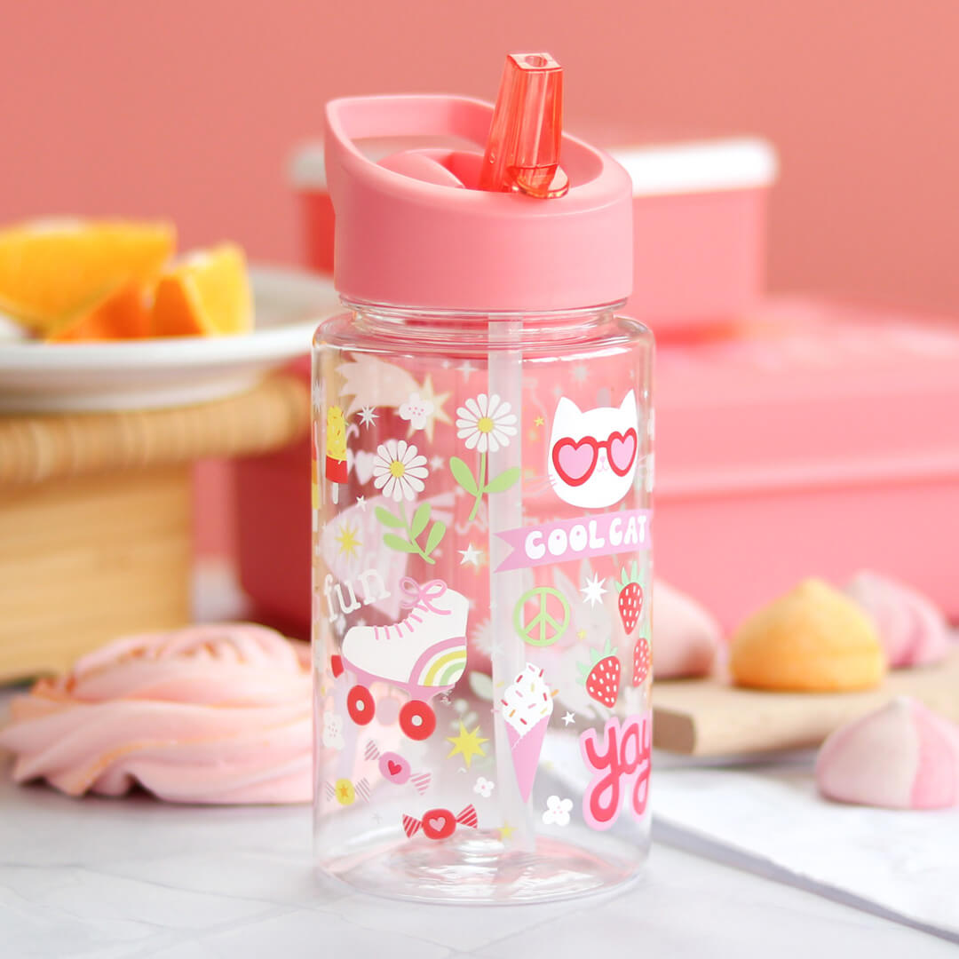 De a little lovely company kinderdrinkfles met roze deksel en rietje, versierd met 'COOL CAT' en rolschaatsen, staat op een tafel met snoepjes en fruit.