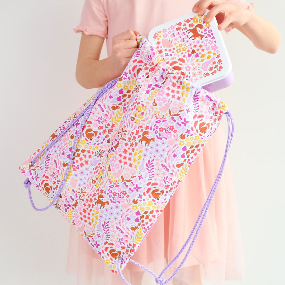 Een kind stopt een lunchbox in de a little lovely company gymtas met bloemen- en dierenprint.