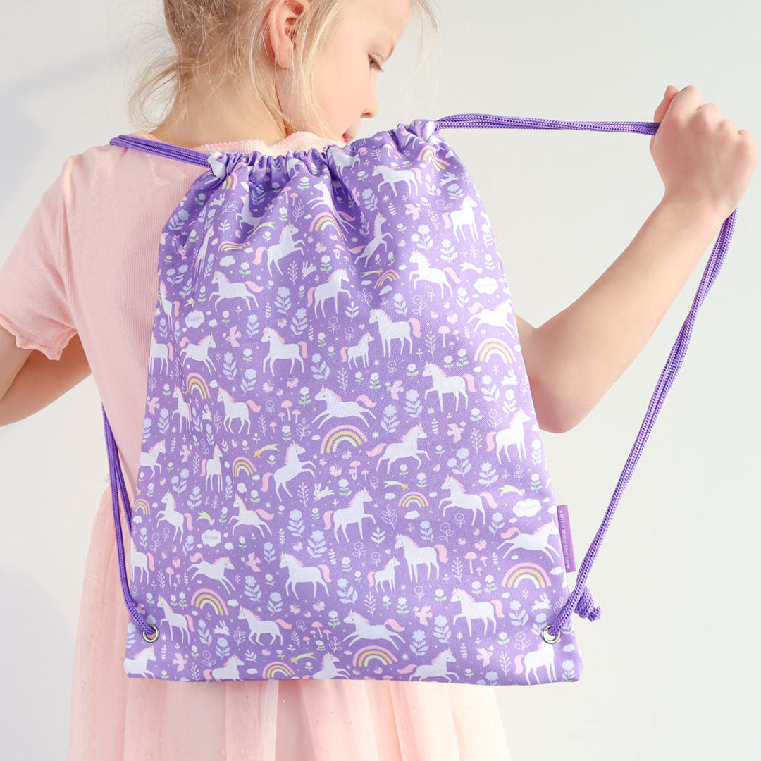 Kind draagt de a little lovely company paarse gymtas met eenhoorn-, bloemen- en regenboogpatroon op de rug.