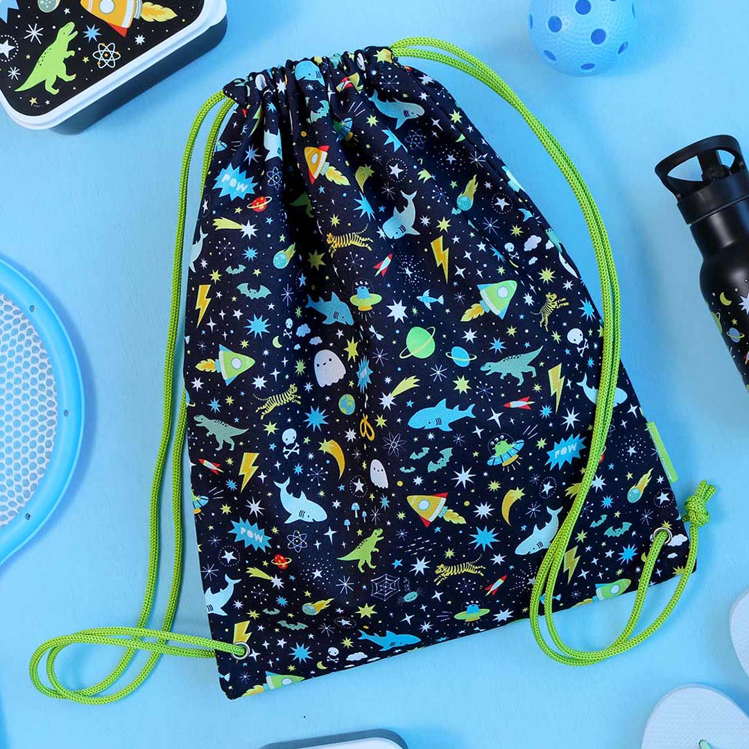 De a little lovely company zwarte kindergymtas met galaxy- en dierenpatroon ligt op een blauwe ondergrond tussen andere spullen.