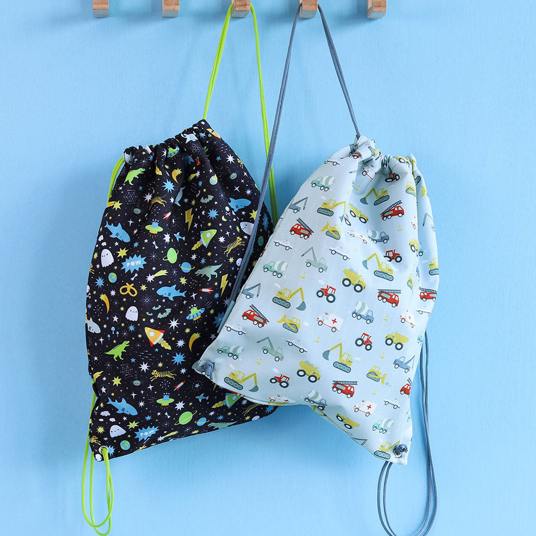 Twee kindergymtassen hangen aan haken, één met galaxy- en dierenpatroon en één met bouwvoertuigenpatroon.