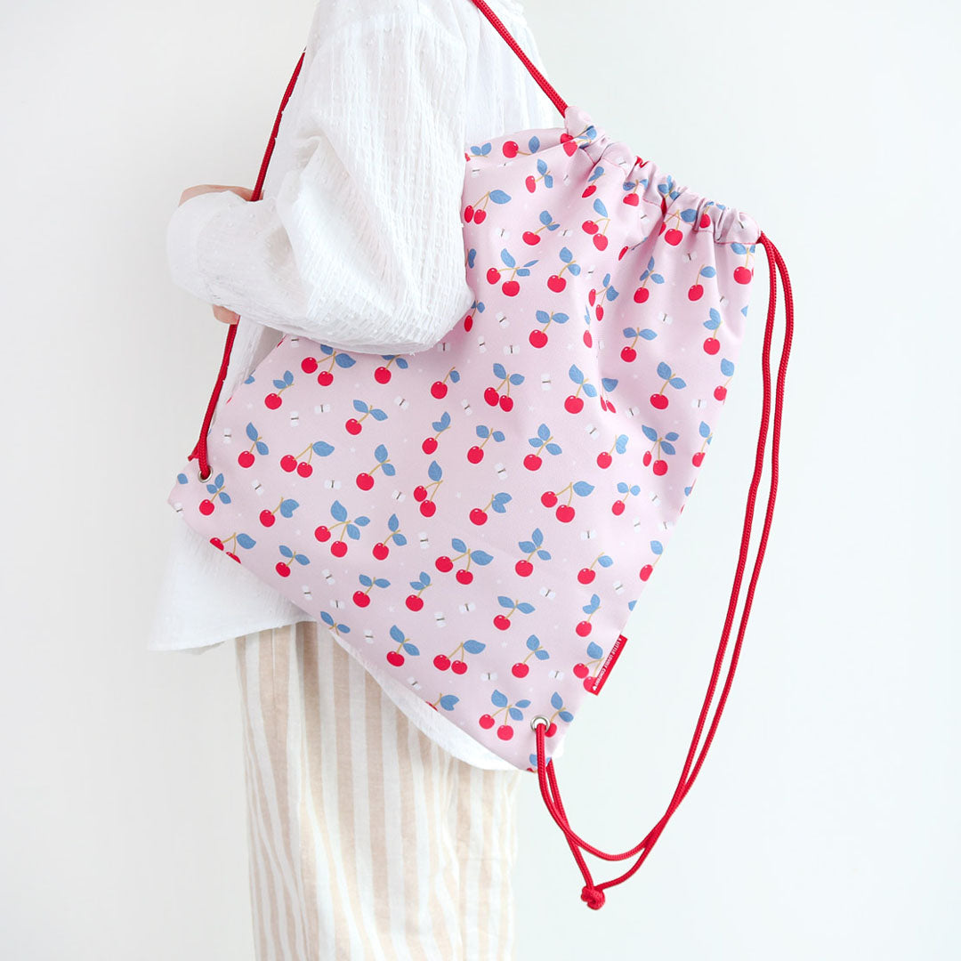 Een persoon draagt de A little lovely company roze gymtas met kersenprint over de schouder.