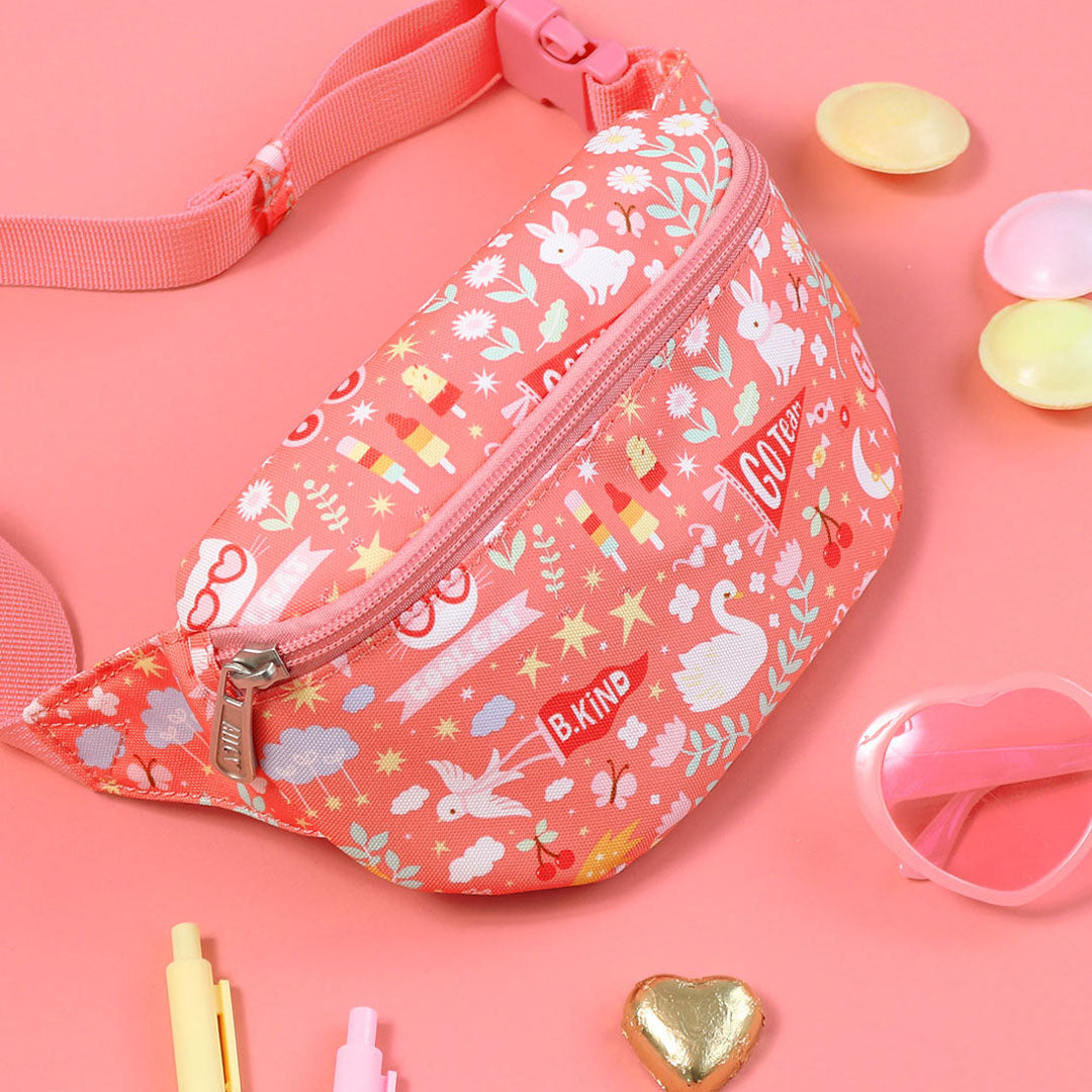 De roze kinder heuptas van a little lovely company ligt op een roze ondergrond met accessoires.