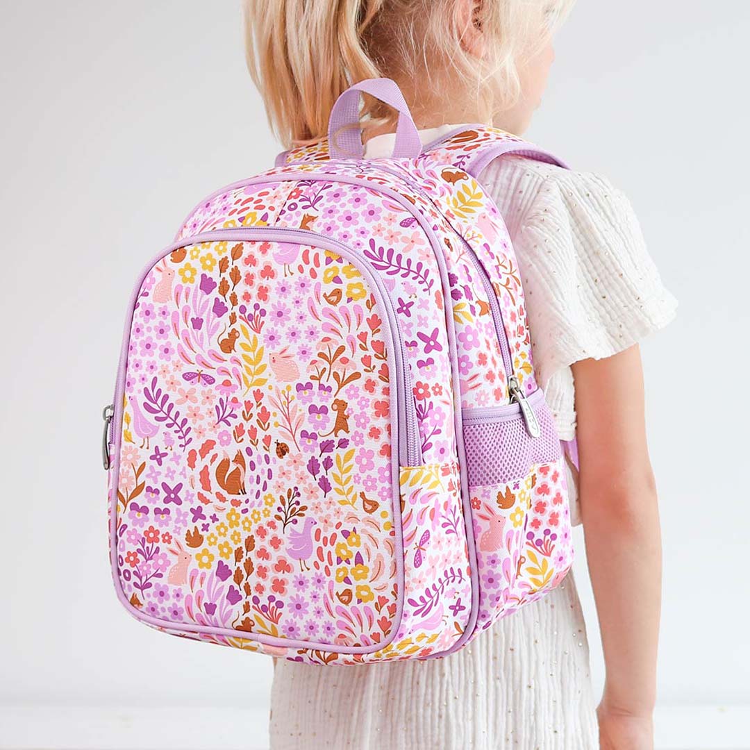 Kind draagt de kinderrugzak met bloemen- en dierenprint op de rug.