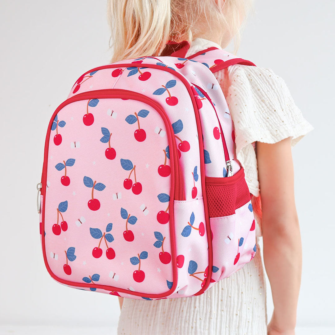 Een kind draagt de roze kinderrugzak van a little lovely company met kersenprint op de rug.