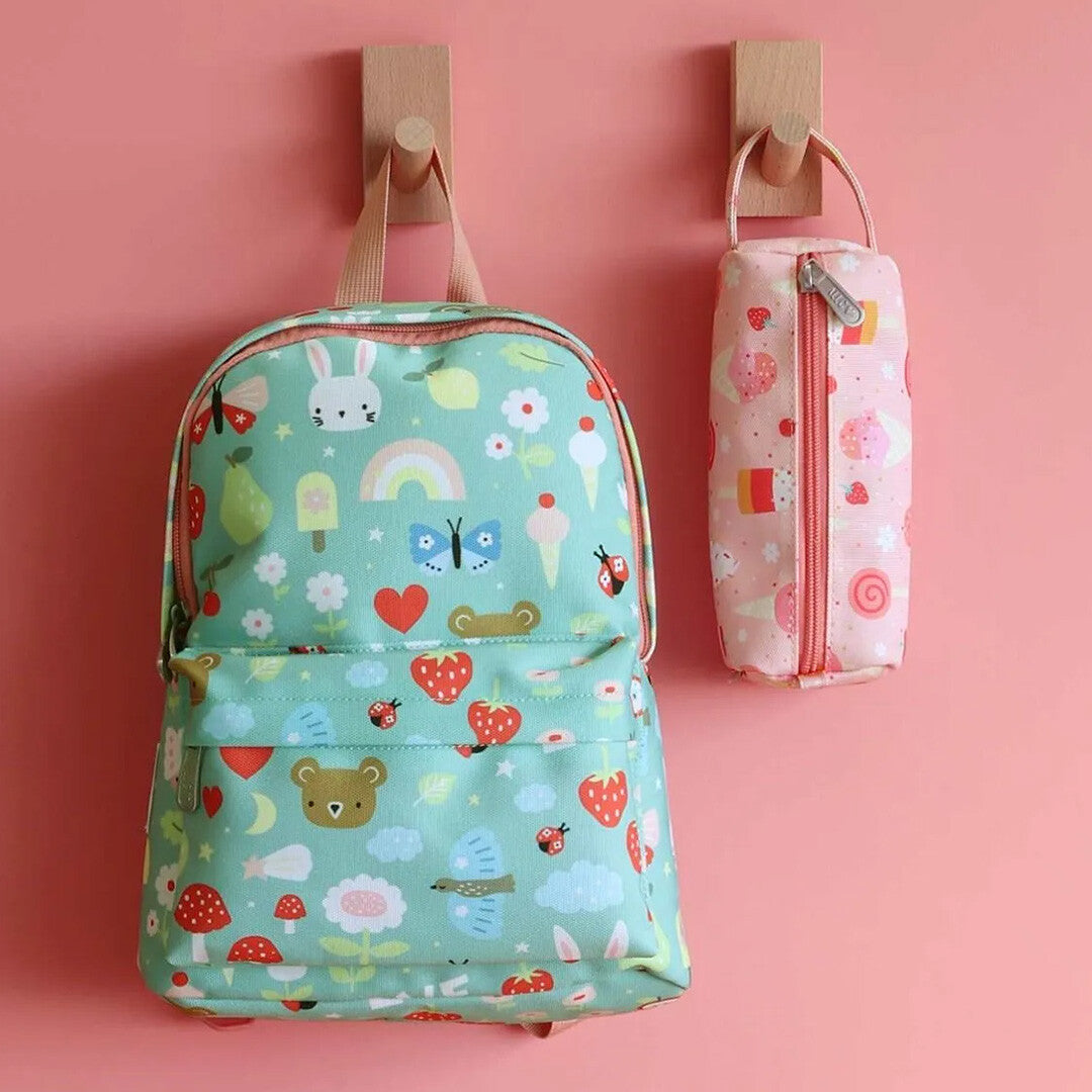 A little lovely company groene kleuterrugzak met dierenpatroon hangt naast een bijpassende roze etui aan een roze muur.