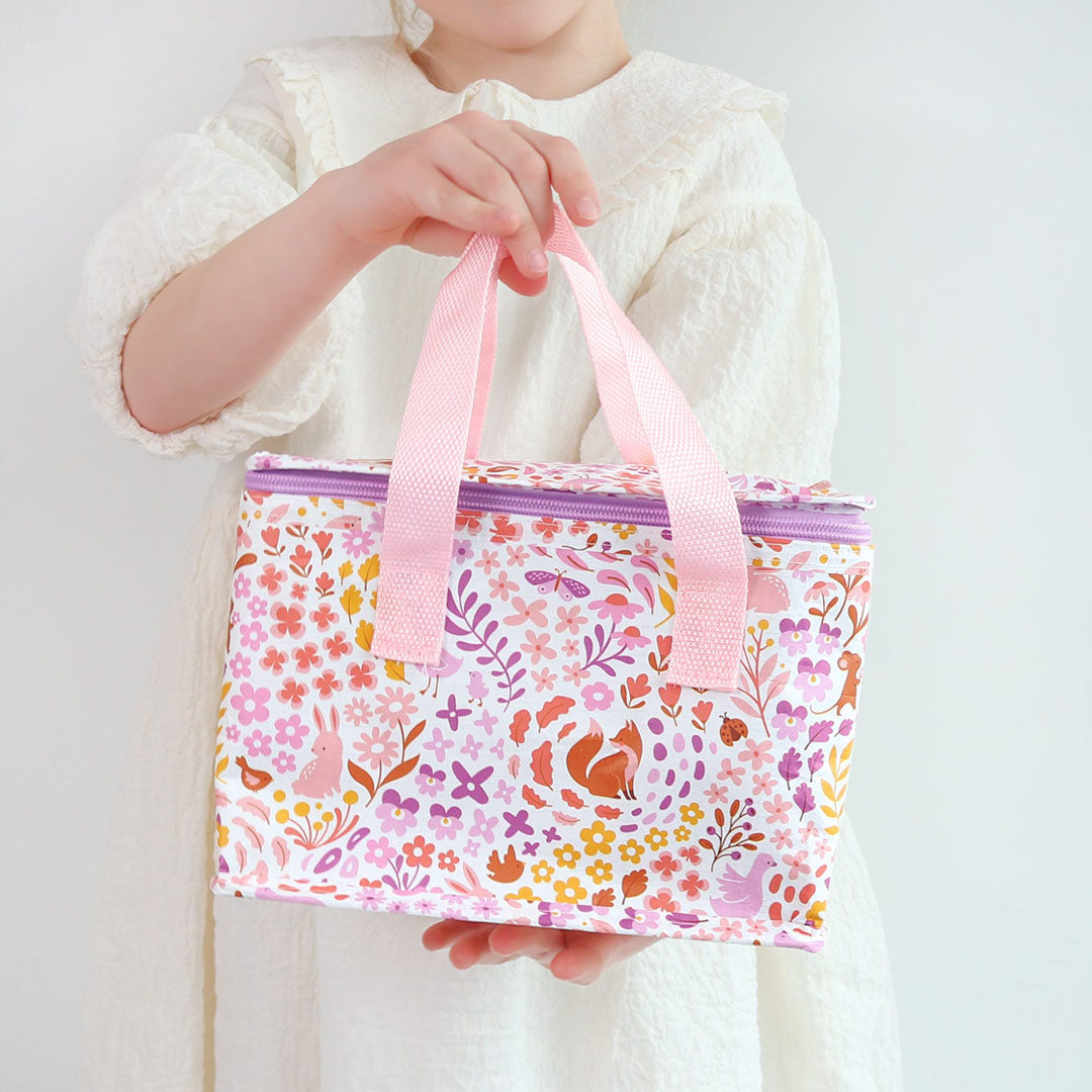 Een kind houdt de a little lovely company koeltas met bloemen- en dierenpatroon vast.