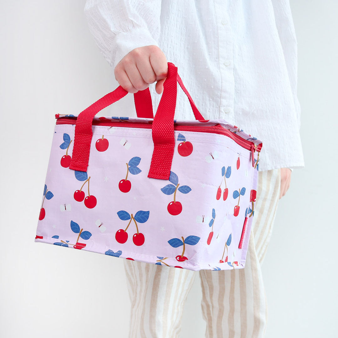 Een persoon houdt de a little lovely company roze koeltas met kersenpatroon vast.