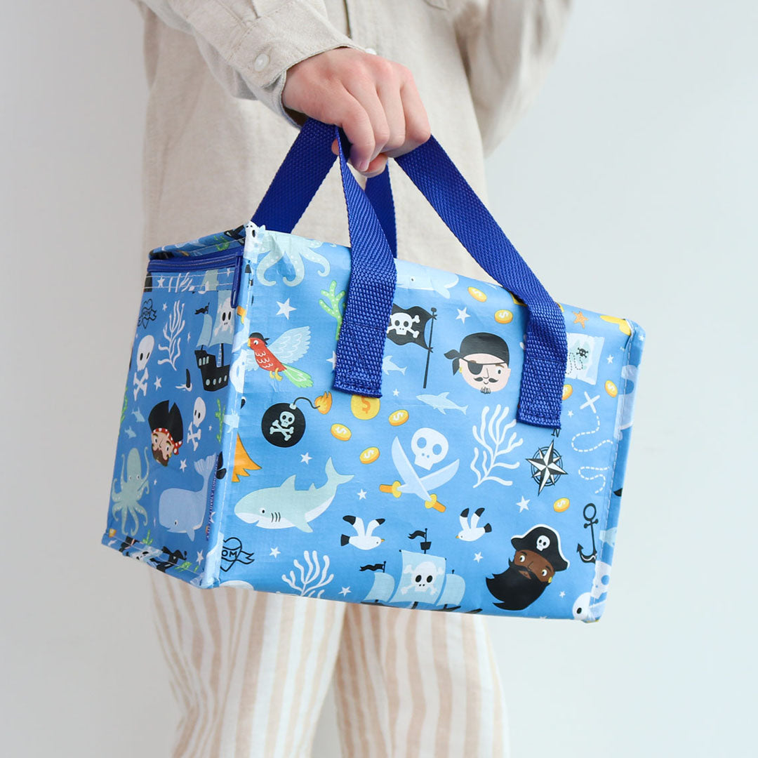 Een persoon houdt de a little lovely company blauwe koeltas met piratenprint vast.