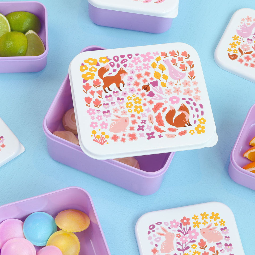 Een open paarse A Little Lovely Company lunchbox met bloemen- en dierenpatroon op de deksel, gevuld met limoenen en meringues.