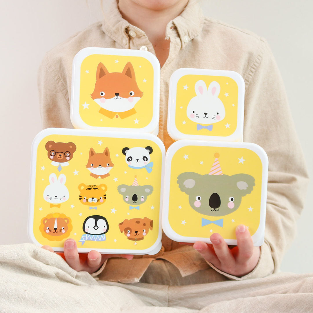 Een kind houdt de A Little Lovely Company broodtrommelset vast met vier gele lunchboxen met dierenvrienden en sterren.