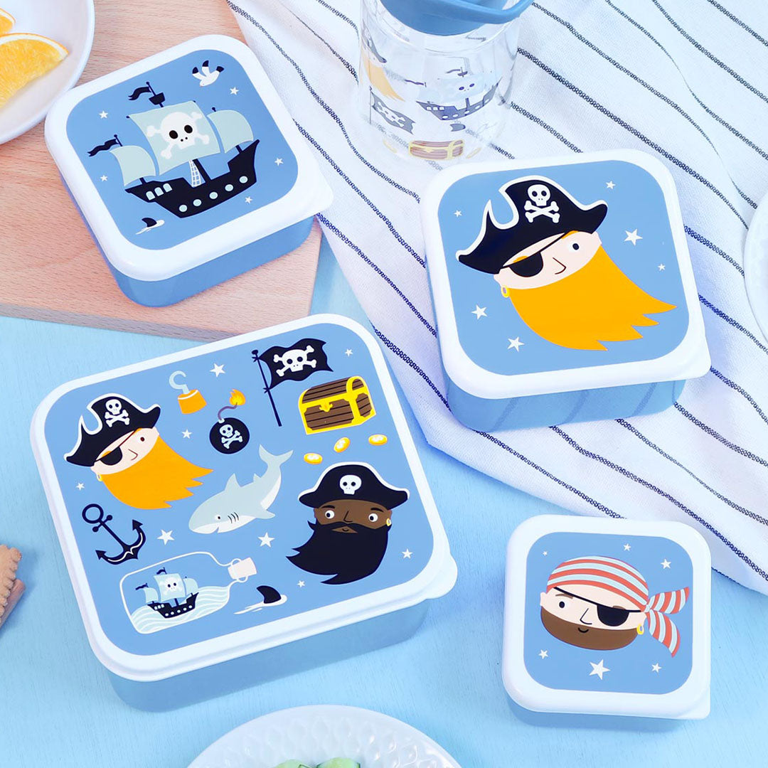 De A Little Lovely Company kinderbroodtrommelset met vier blauwe lunchboxen in piratenthema, verspreid op een tafel met een waterfles.
