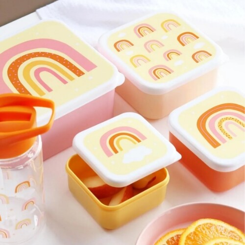 a little lovely company broodtrommelset met vier plastic lunchboxen met regenboogpatronen, waarvan één open met appelstukjes, naast een waterfles.