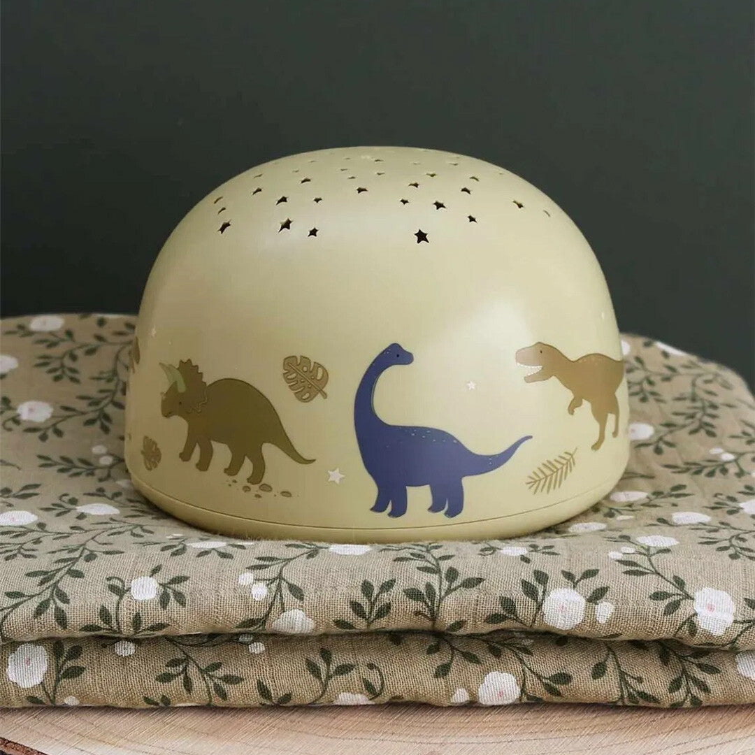 A little lovely company beige nachtlamp en sterprojector met dinosaurusafbeeldingen op een gevouwen doek.