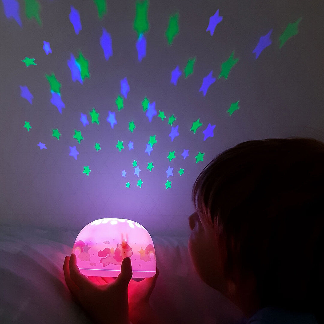 Een kind kijkt naar de a little lovely company nachtlamp en sterprojector die groene en blauwe sterren projecteert.