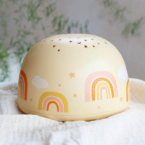 A little lovely company beige nachtlamp en sterprojector met regenboog- en sterpatronen op een witte doek.