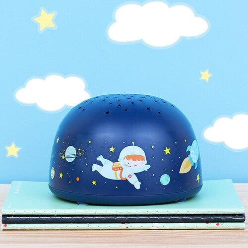 De A little lovely company nachtlamp en sterprojector met ruimtefiguren staat op boeken voor een blauwe muur met wolken.