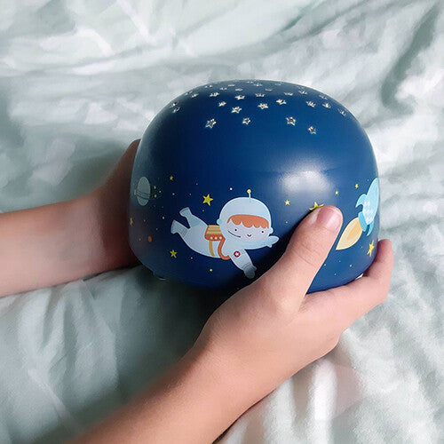 Kinderhanden houden de A little lovely company nachtlamp en sterprojector vast, versierd met een astronaut en een raket.