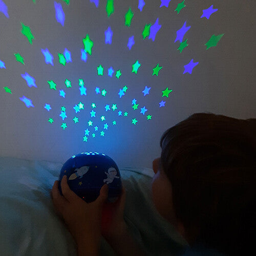Een kind kijkt naar de A little lovely company nachtlamp en sterprojector die groene en blauwe sterren op de muur projecteert.