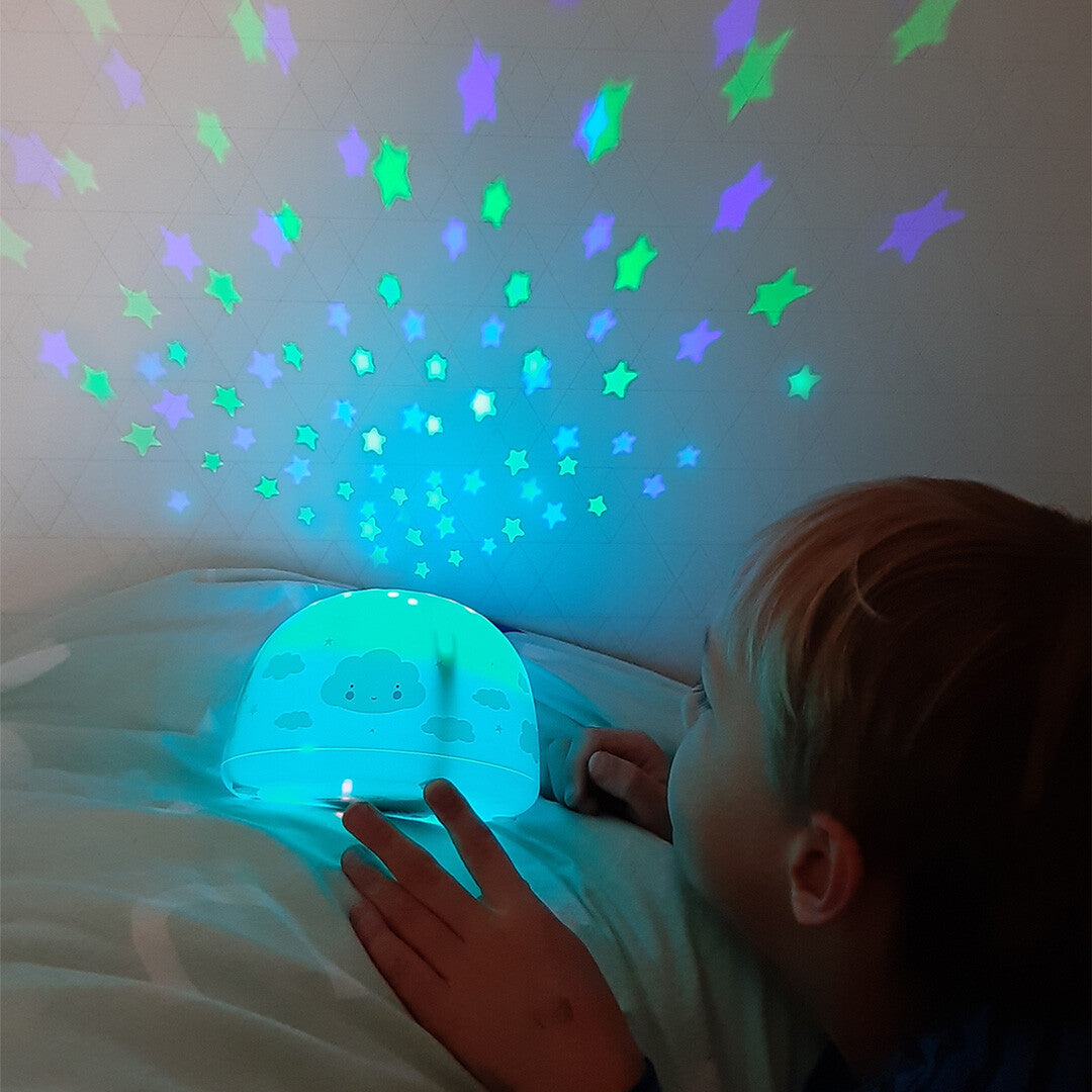 Een kind kijkt naar de a little lovely company sterprojector die blauwe en groene sterren op de muur projecteert.