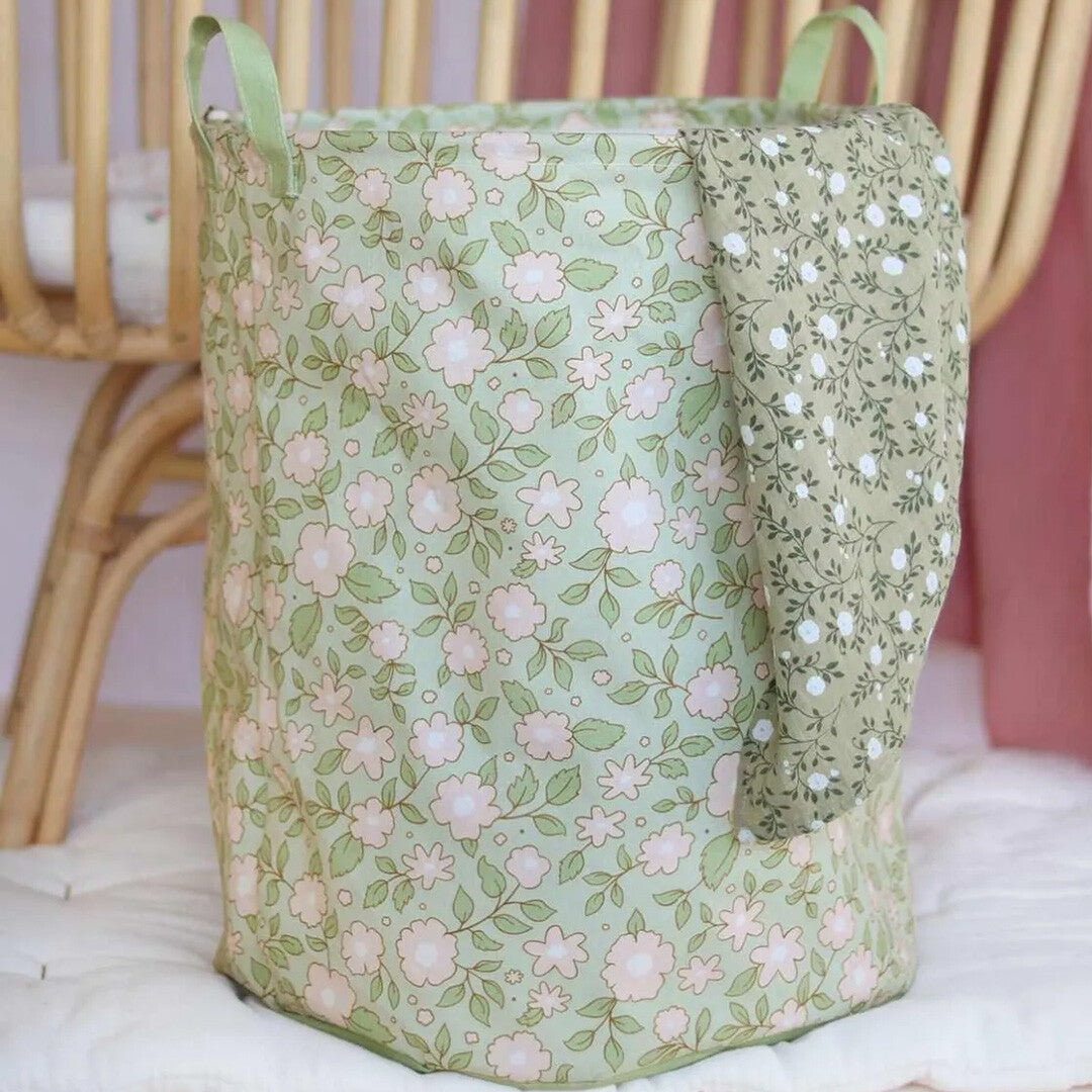 a little lovely company opbergmand met lichtroze bloemenpatroon, staand naast een wieg met een doek eroverheen.