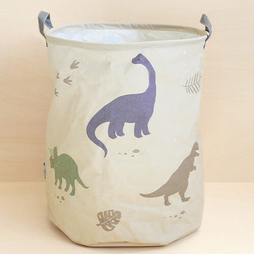 a little lovely company beige opbergmand met dinosaurussen en bladeren op een houten ondergrond.
