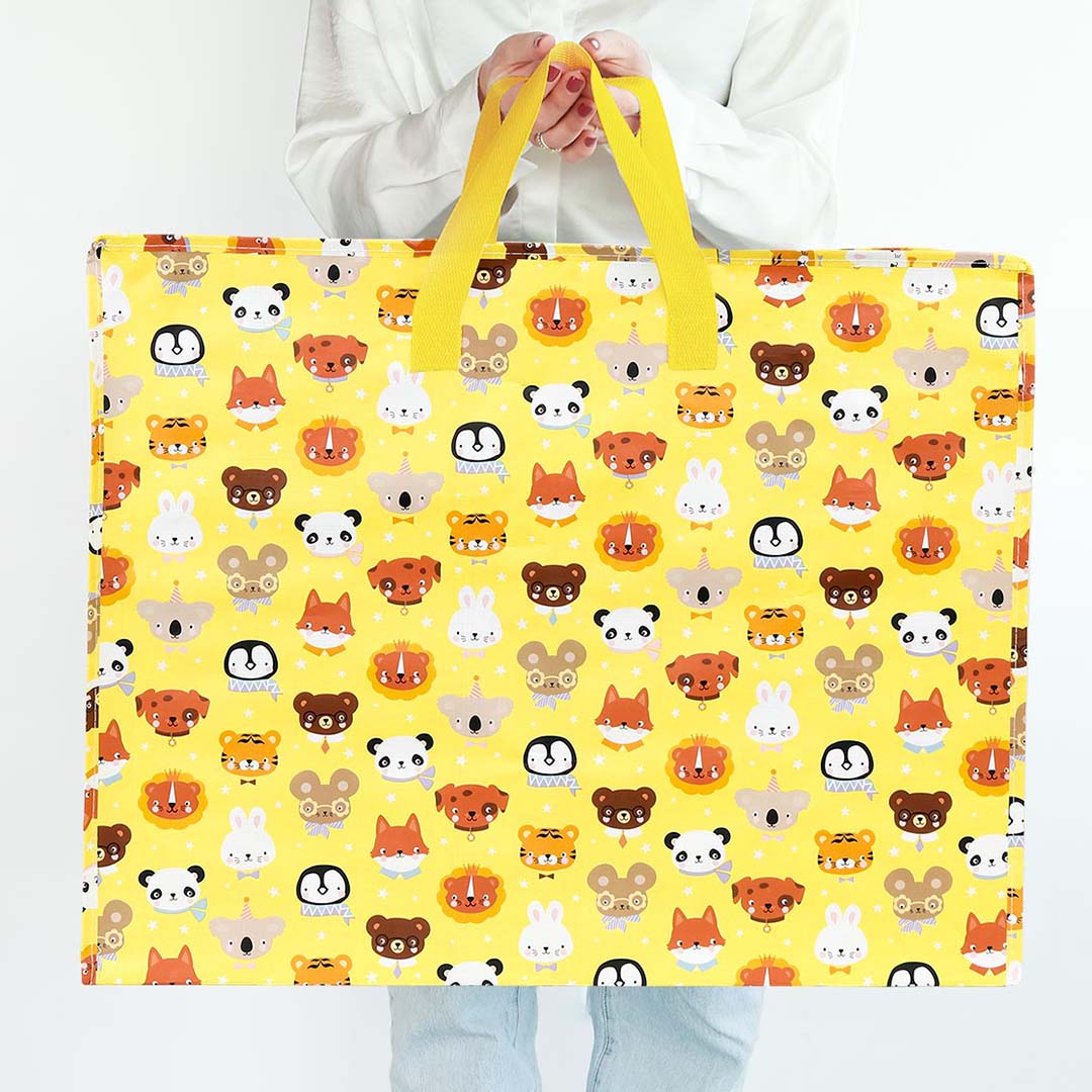 Een persoon houdt de a little lovely company opbergtas dierenvriendjes, een gele plastic opbergtas met een patroon van diverse dierenhoofden, voor zich uit.